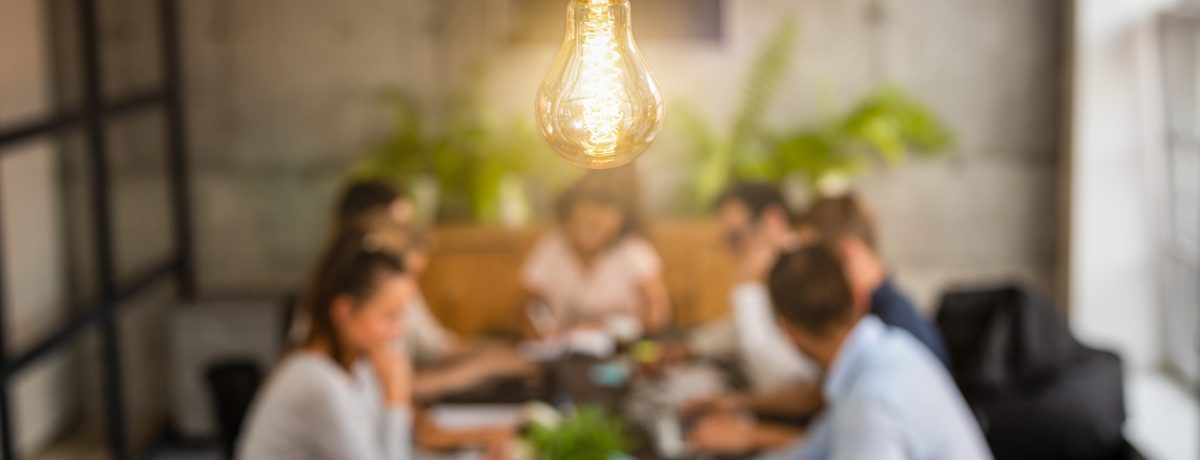 The PESO Model blog image shows a team meeting to review reports. The meeting room has a warm light above and a dark wood desk. Plants behind the team.