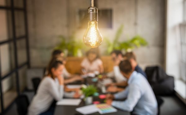 The PESO Model blog image shows a team meeting to review reports. The meeting room has a warm light above and a dark wood desk. Plants behind the team.