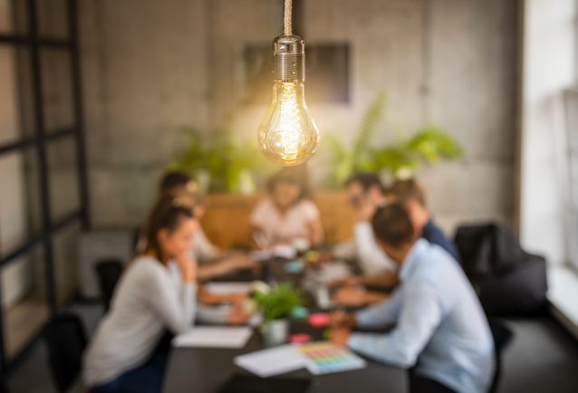 The PESO Model blog image shows a team meeting to review reports. The meeting room has a warm light above and a dark wood desk. Plants behind the team.