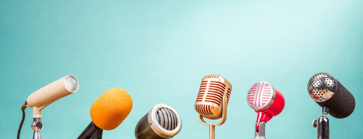 A row of different styles of microphone on a wooden table with a mint green background for the interview tips blog.