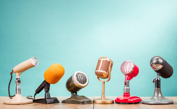 A row of different styles of microphone on a wooden table with a mint green background for the interview tips blog.