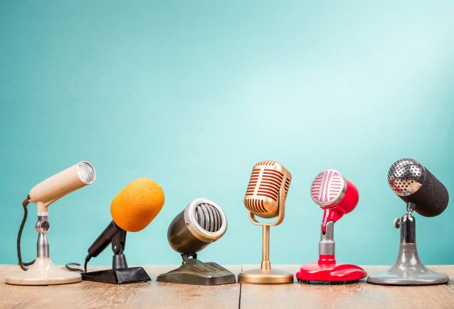 A row of different styles of microphone on a wooden table with a mint green background for the interview tips blog.