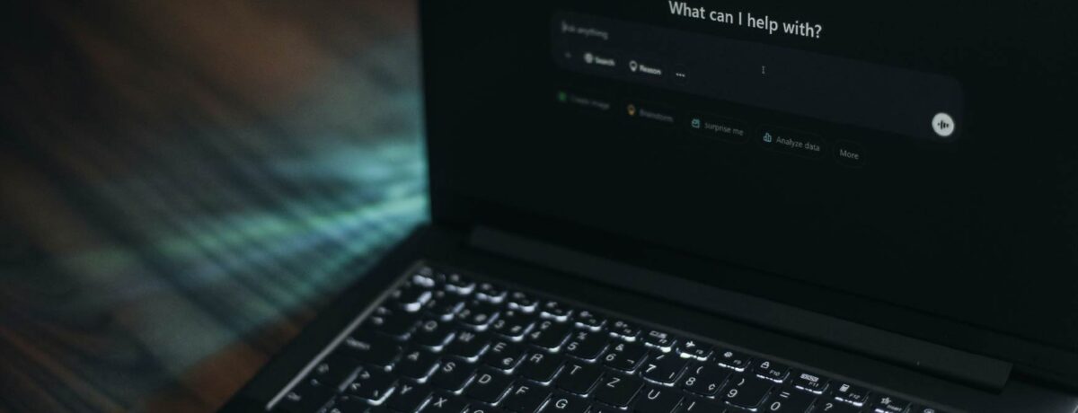 A dark image showing a laptop at an angle with the screen showing an AI chat bot landing page. The ChatGPT dashboard reads: "what can I help with?" and the cursor is ready in the prompt box.